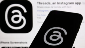 Threads logo displayed on a phone screen and Threads on App Store displayed on a screen in the background in this illustrated photo by Jakub Porzycki with NurPhoto.